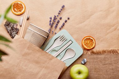 Sustainable tableware cutlery, cardboard cups made from natural materials and paper bag on crumpled paper. Zero waste, eco-friendly lifestyle.