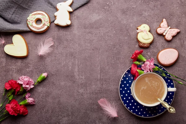 Easter aesthetic coffee time. Glazed cookies, coffee cup, feathers, aster flowers flat. lay. Spring stylish background with copy space.