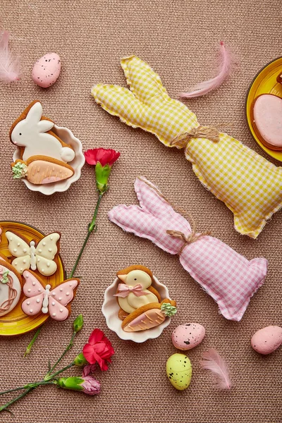 Spring Easter aesthetic background flat lay. Glazing Easter cookies, handmade bunny toys, pink flowers with feathers