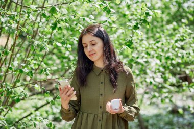 Kulaklıklı telefon kullanan genç bir kadın - müzik dinlemek, online toplantı yapmak veya arkadaşlarla sohbet etmek, İnternet kursunu dinlemek. Rahatlama ve rahatlama konsepti.