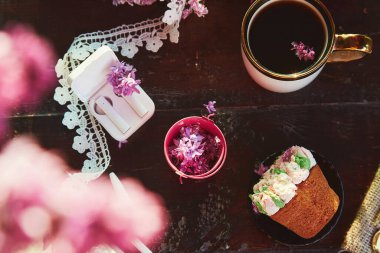 Estetik pembe çiçekli kek, masada kahve fincanı. Kablosuz kulaklıklar, müzik dinlemek, sesli kitap konsepti. Baharda açık havada leylak çiçekleri seriliydi. Katman arkaplanı.