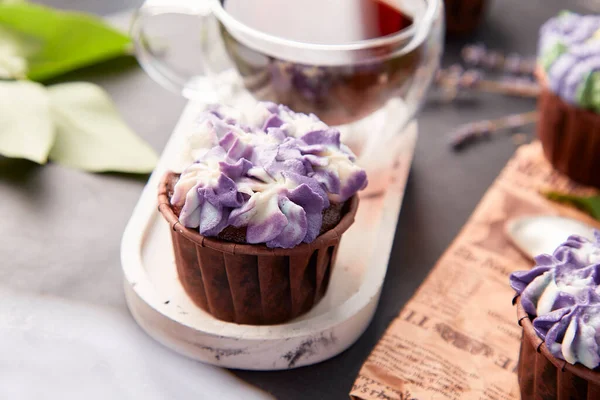Purple aesthetics trendy floral cupcake and cup of coffee close up. Violet french no sugar dessert with lilac flowers.