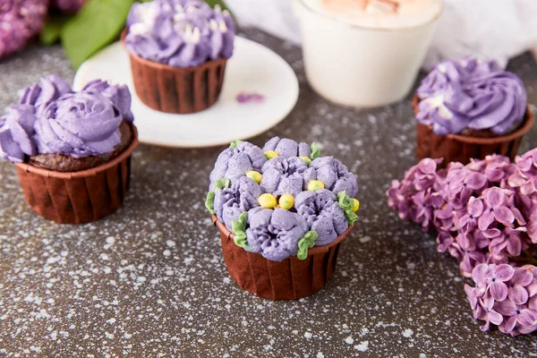 Floral purple cupcakes using trend Dreamy Escapism. Aesthetics desserts, coffee cup and lilac flowers background. Catering food.