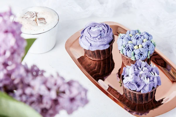 节假日餐桌 金盘上的紫色法国纸杯蛋糕 咖啡和丁香花平铺在地上 — 图库照片