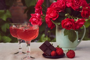 Estetik yaz natürmort. Kırmızı köpüklü çilek şampanyası, gül çileği ve çikolata. Yazlık masa ayarları açık
