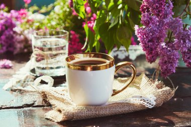 Leylak çiçeklerinin arasında bir fincan kahveyle kahve molası. Çiçekli yaratıcı kek. Estetik kır evi temel yaşam tarzı.