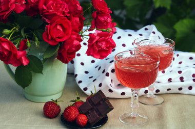 Bir bardak kırmızı çilek köpüklü şarap, çilek ve çikolata. Gül buketi. Estetik yaz masa ayarları