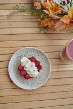 Estetik sağlıklı sonbahar öğle yemeği. Ahşap masada pembe çilekli smoothie ve Fransız turtası. Dikey fotoğraf.