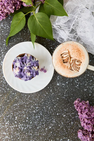 Aesthetic trendy purple cake, cup of coffee with melted marshmallow top view among lilac flowers. French no sugar dessert. Copy space.