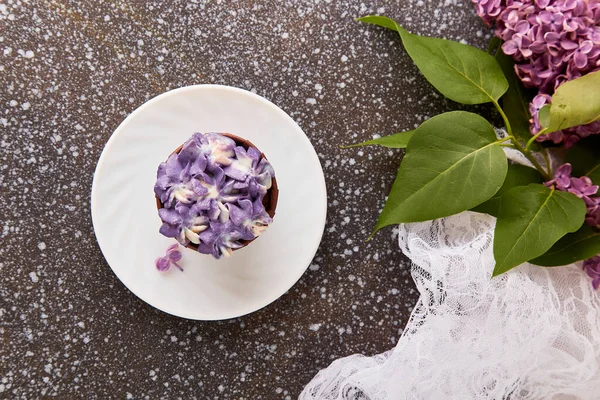 Aesthetics purple floral cake among lilac flowers top view. Spring background.
