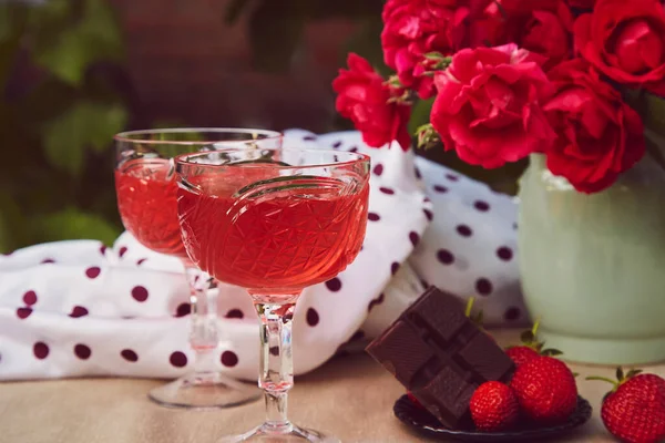 stock image Couple glasses of red sparkling strawberry wine with roses outdoor, strawberry and chocolate. Aesthetic summer table settings