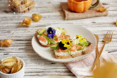 Sağlıklı karamsar kahvaltı. Hafif tuzlu somon, yenilebilir çiçekler, avokado ve roka ile tost. Bir fincan kahve ve kış kirazı. Atmosferik sonbahar yemekleri.