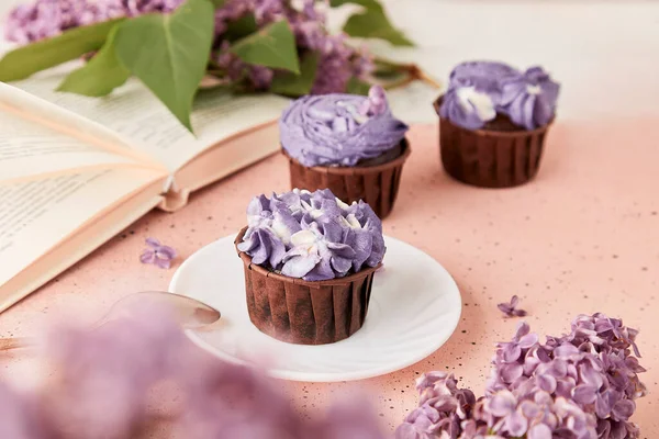 Aesthetic french purple floral cupcakes using trend Dreamy Escapism. Coffee time among lilac flowers, reading the book. Leisure and relax coffee time.