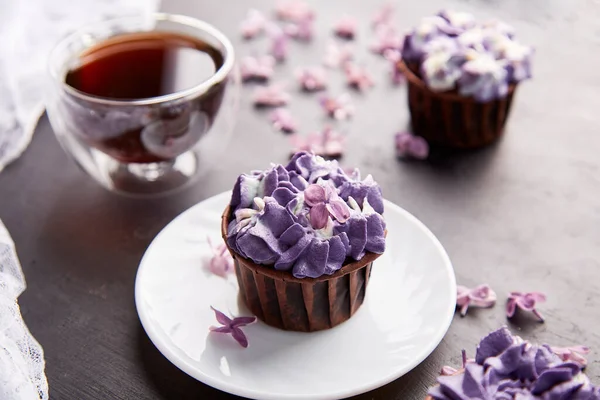 Aesthetics purple trendy floral cupcakes with cup of coffee. Violet sweet no sugar dessert among lilac flowers.