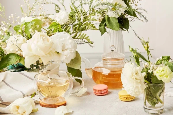 Aesthetic tea time, herbal tea and macaron desserts in biophilic interior among white flowers. Natural herbal tea - sustainable eco-friendly lifestyle.