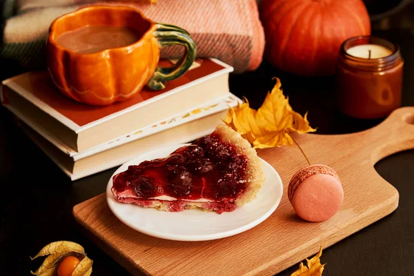Aesthetics cherry pie, cup of coffee in shape of pumpkin, macaroons, candles and fragrant leaves. Hygge home aesthetic.