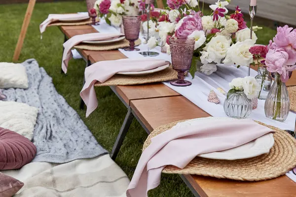 Aesthetics pink cozy picnic, served table with pink flowers bouquets, pillows, candles decor shells in the garden.