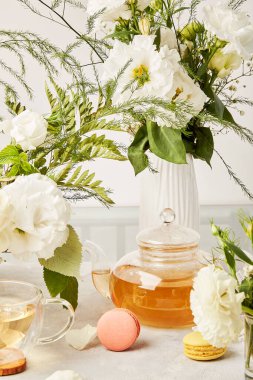 Estetik çay saati, çaydanlık, bitkisel çay ve beyaz çiçeklerin arasında biyofilik iç kısımda makarna tatlısı. Kadınsı sakin yaşam tarzı.