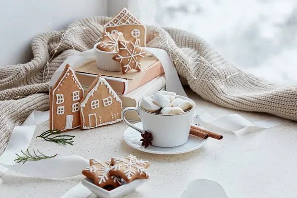 Warm marshmallows cocoa with homemade ginger cookies in shape of cute homes and snowflakes. Aesthetic female Christmas background.