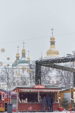 Kyiv, Ukrayna - Ocak 2022: Karlı bir günde Noel pazarı - Tapınağın altın kubbeleri, insanlar, dükkanlar ve dekorasyonlar. Savaştan önce bayram.