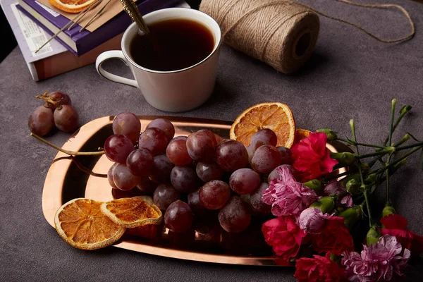 Spring aesthetic cozy still life snacks with grapes, cup of coffee and flowers on the golden tray.