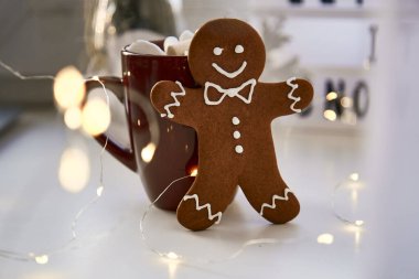 Homemade gingerbread cookie and blurred bokeh background close up. Festive Christmas decorations with hot drink and marshmallows. Aesthetic Christmas atmosphere, home coziness, warmth concept