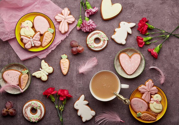 Aesthetic Easter background complete decorated cookies, coffee cup, feathers and aster flowers flat lay. Spring background