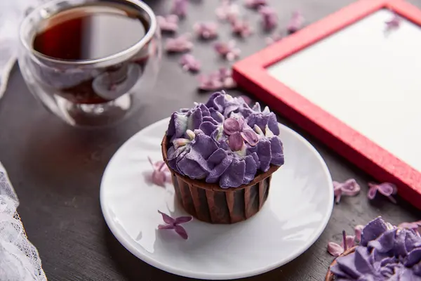Purple floral cupcake using trendy Escapism trend. Frame mock up, cup of coffee among lilac flowers.