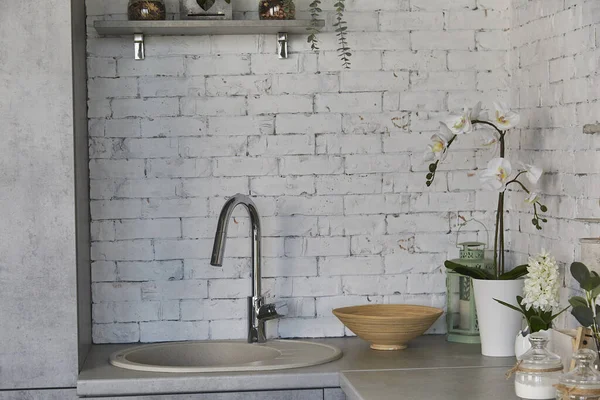 Trendy kitchen design featuring sink and greenery accents. White brick texture.