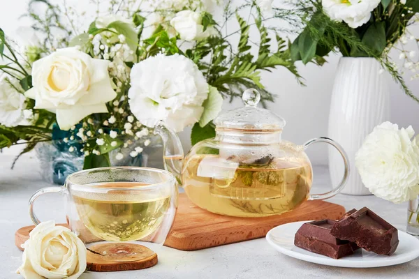 Aesthetic tea time, teapot, green tea and chocolate in biophilic interior among white flowers. Feminine calm lifestyle, cozy home concept.