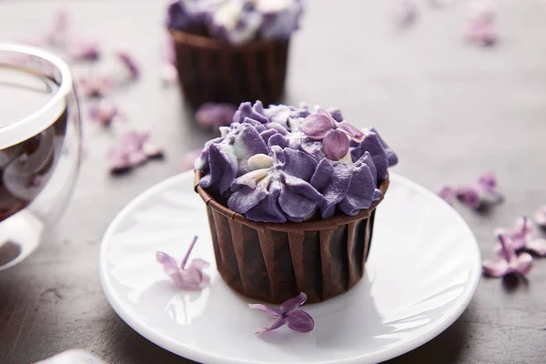 Floral purple cupcake close up using trend Dreamy Escapism. Desserts, coffee and lilac flowers background. Aesthetics food.