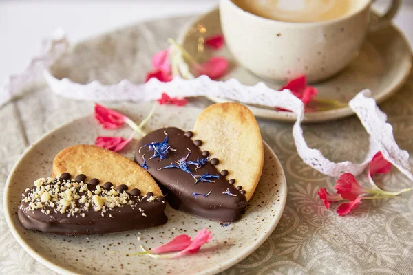 Aesthetic vegan cookies in heart shape among flowers and cup of coffee. Romantic holiday food background.
