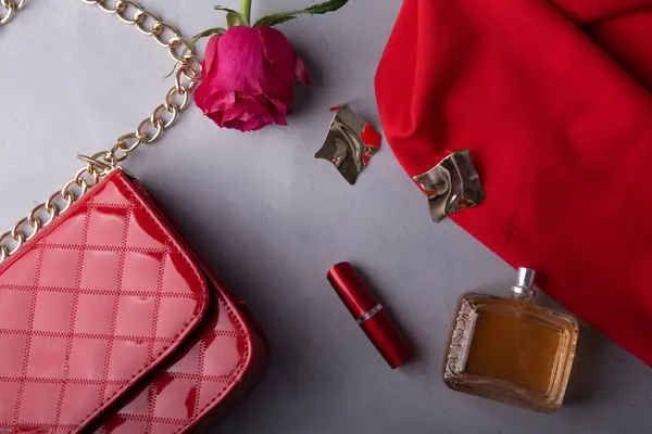 Essentials with perfume and lipstick for a sophisticated look among roses.
