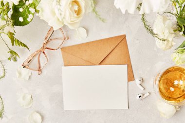 Estetik kadınsı düz bardaklar, çay fincanı ve el işi kağıt zarflı kulaklıklar selamlama için, beyaz çiçeklerin arasında metin