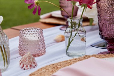 Piknik masası dekorasyonu, çiçek aranjmanı, kabuklar. Çiçekler ve mumlarla donatılmış rahat bir ortam..