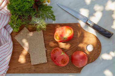 Güneşli bir günde dışarıda yemek hazırlıyorum. Domates, yeşillik ve kepekli çıtır ekmek. Sağlıklı beslenme. Veganlık, Keto, Bitki temelli, Paleo, Fodmap diyet konsepti. Boşluğu kopyala