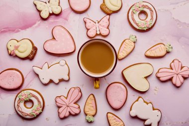 Pastel Paskalya arkaplanı. Kurabiyelerin arasında kahve fincanı. Pembe arka planda Paskalya 'nın parlak sembollü bahar kartı yatıyordu.