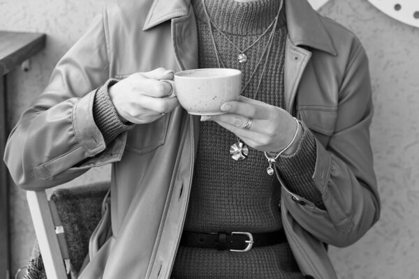 Close up woman with blue manicure holds a coffee cup with cappuccino. Black and white background.