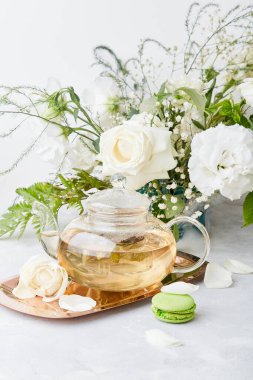 Estetik masa düzenlemesi. Yeşil çay demliği, badem kurabiyesi tatlısı, beyaz güller ve Eustomas. Kendine zaman ayır, dinlen, çekirdek, yavaş yaşam konsepti