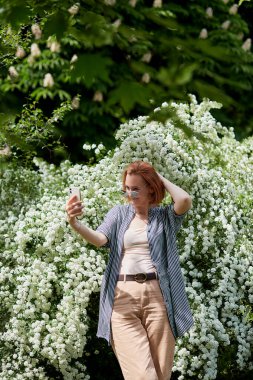 Tamamen beyaz çiçeklerle serbest blog yazarı yaşam tarzı çiçek açıyor - genç kızıl saçlı kadın selfie çekiyor.
