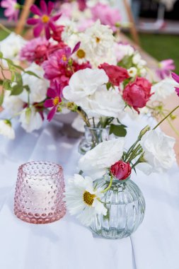 Pembe mum ve pembe ve beyaz çiçek buketleri. Sıcak atmosfer, yaz piknik masası..