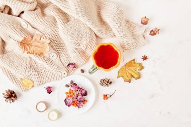 Autumn-Inspired sweater weather background - pumpkin tea cup with hot beverage, among dry roses leaves and candles clipart