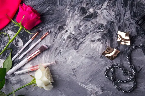 stock image Beauty essentials with makeup brushes and vibrant roses on a textured abstract backdrop.