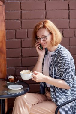 Şehir hayatı. Kahve molası sırasında telefonuna gülümseyen bir kadın. Yoğun gününün tadını çıkarıyor.