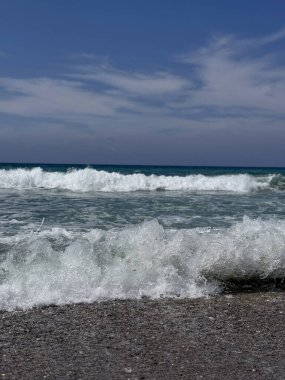Parlak güneş ışığı altında ışıldayan deniz dalgaları. Işıldayan okyanus yüzeyi, güneşte parlayan yumuşak dalgalarla, sahilde sakin bir yaz gününün güzelliğini yakalıyor.