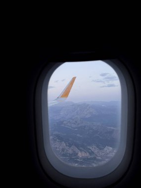 Kanat, Bulutlar ve Aşağıdaki Peyzaj Uçağı Pencere Manzarası. Seyahat, içgözlem ve uçsuz bucaksız manzaralarla insan bağlantısı, karamsar, sinematik bir atmosferde yakalanmış.