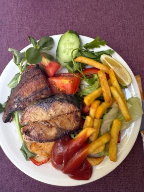 Fırında balık, patates, patates, yeşillik ve ketçap ile dolu büyük tabak.