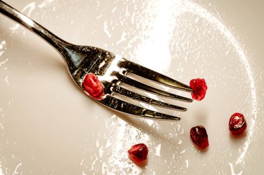 Minimalist Çatallı Sürüngen Nar kıvılcımı. Dağınık nar tohumlarıyla beyaz bir tabakta dinlenen tek çatal..