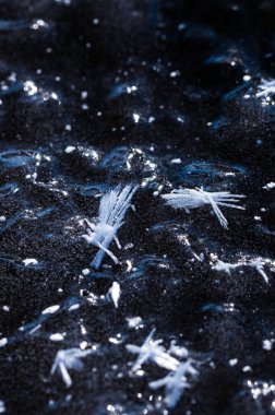 Shimmering frost crystals form intricate patterns on the dark ground, creating a contrast between the bright ice structure and the deep winter background. clipart