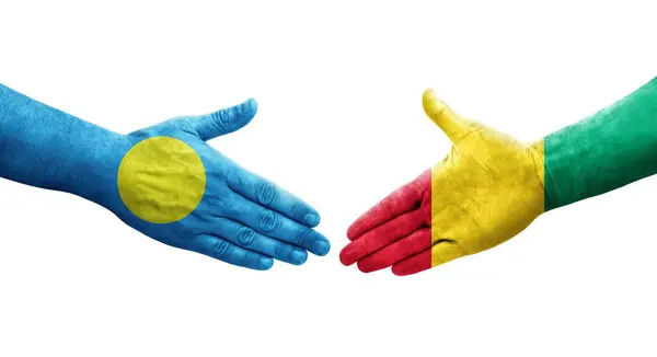 stock image Handshake between Guinea and Palau flags painted on hands, isolated transparent image.